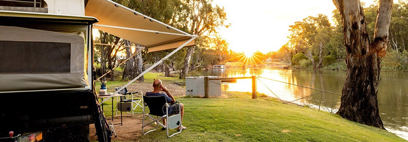 man sitting outside of a caravan enjoying a sunset over a river